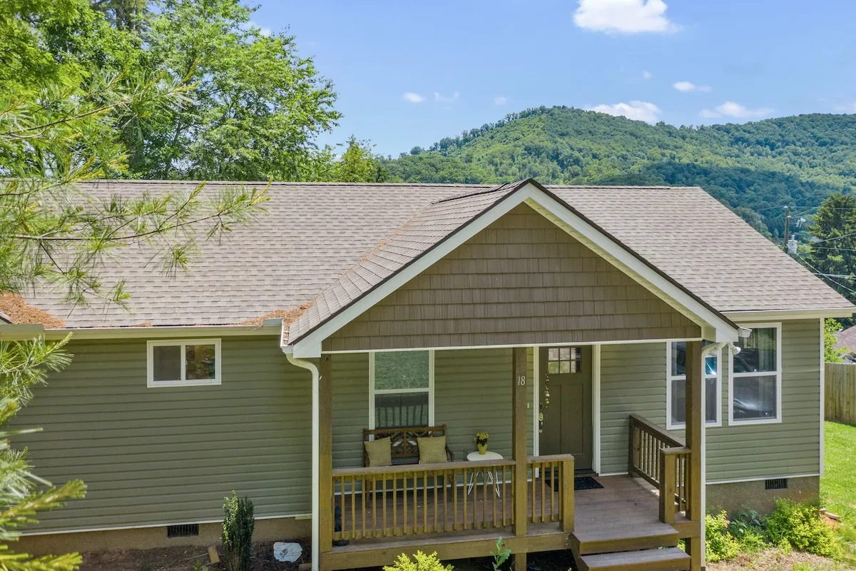 Alondra's Home, a sage-green cottage with a covered porch, below wooded mountains in Candler, NC