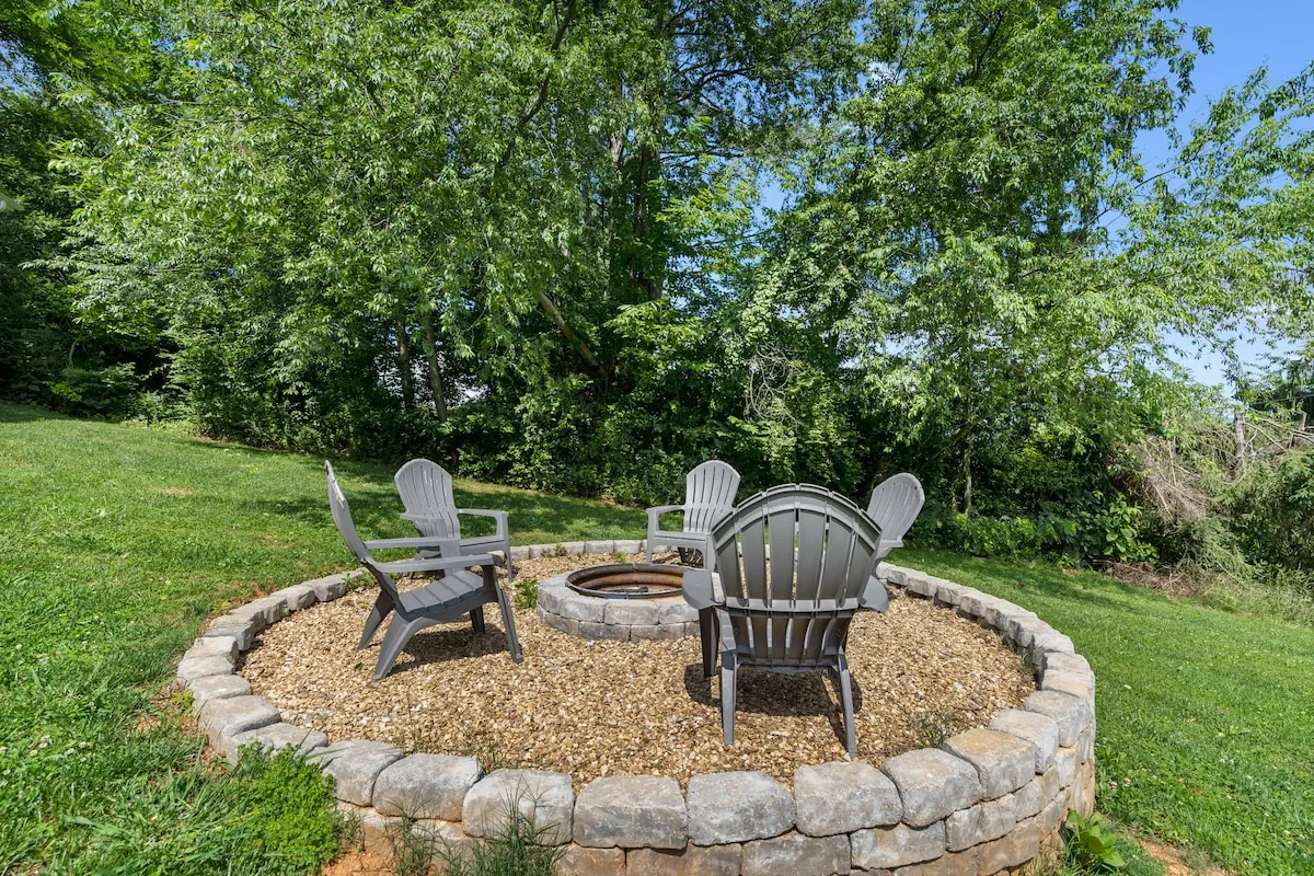Stone fire pit ringed with Adirondack chairs in the backyard