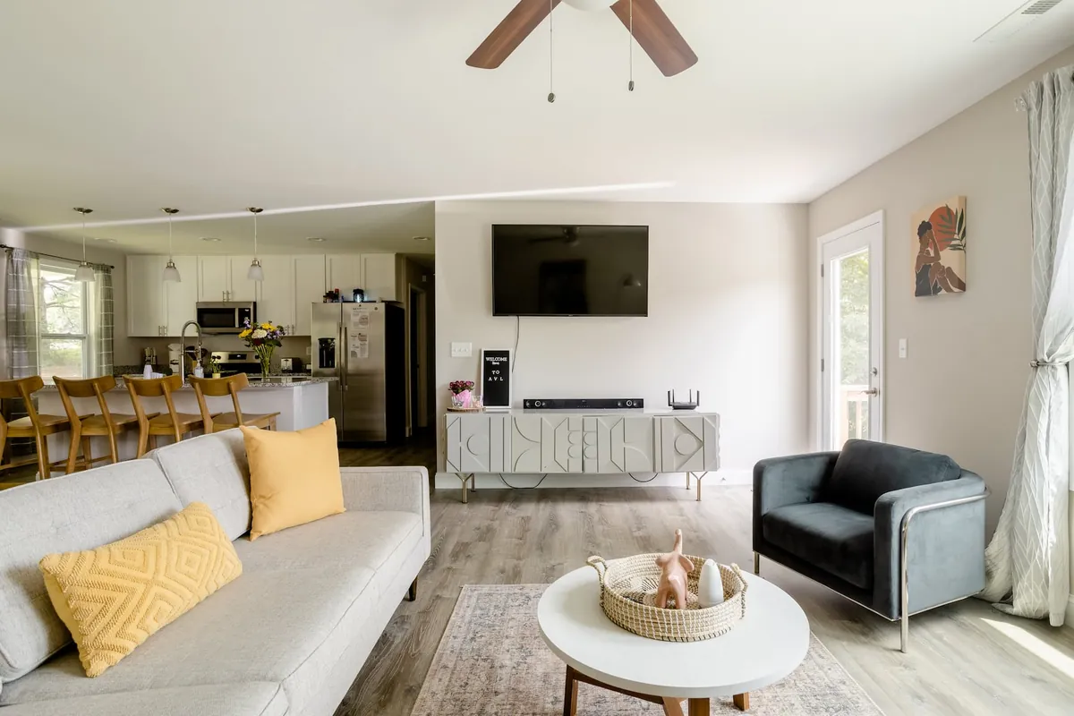 Open living room with a sofa, armchair and TV, opening into the kitchen